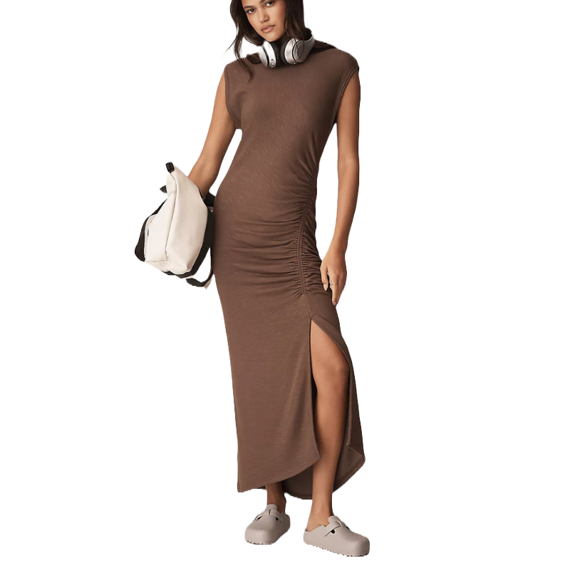 A person wearing a brown, sleeveless, ruched dress with a side slit, beige clogs, and a pair of headphones. They are holding a white and black bag.