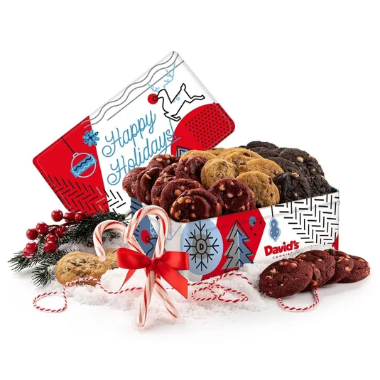 A festive gift tin labeled \“Happy Holidays\“ containing an assortment of 24 cookies, including flavors like chocolate chip, red velvet with white chips, and double chocolate, decorated with candy canes, pine branches, and berries.