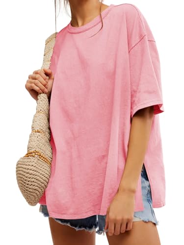 A person wears a loose-fitting pink T-shirt, denim shorts, and carries a woven bag.