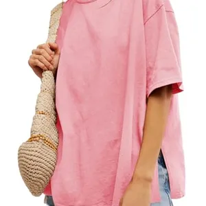 A person wears a loose-fitting pink T-shirt, denim shorts, and carries a woven bag.