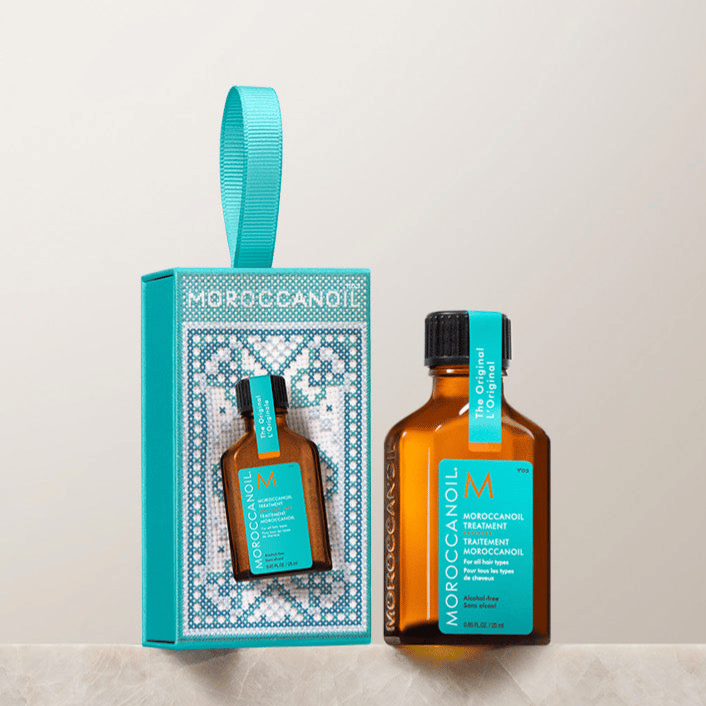 A small bottle of Moroccanoil Treatment and its packaging, featuring a teal and brown color scheme with a decorative design, is displayed on a marble surface.