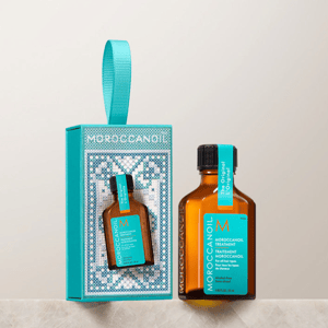 A small bottle of Moroccanoil Treatment and its packaging, featuring a teal and brown color scheme with a decorative design, is displayed on a marble surface.