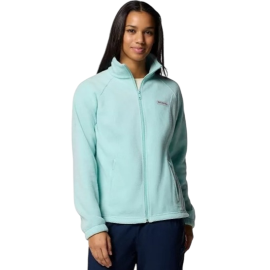 A woman is wearing a light blue zip-up fleece jacket with a high collar, featuring a small logo on the chest. She pairs it with dark pants.