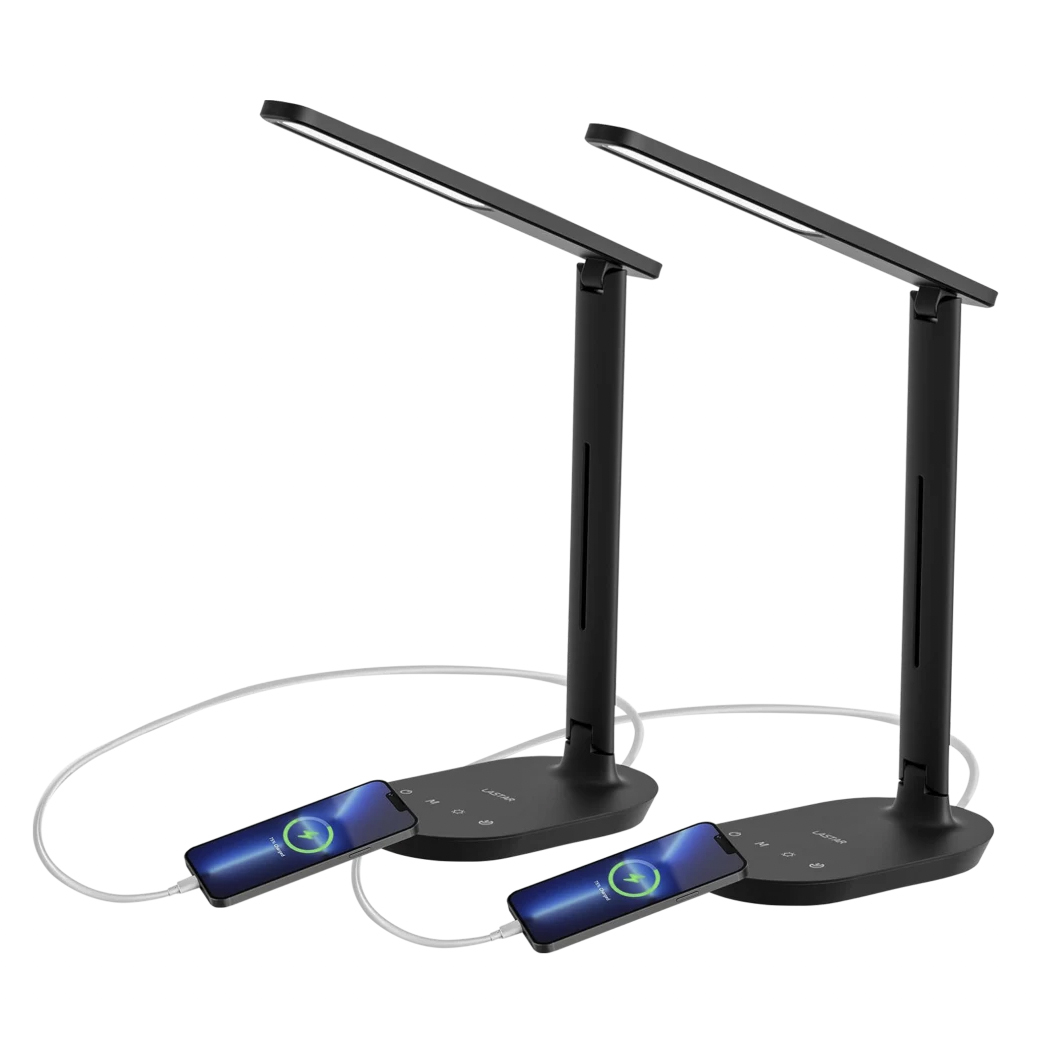 Two black LED desk lamps with built-in charging ports, each charging a smartphone with visible cables. The lamps have a sleek, modern design with touch controls on the base.