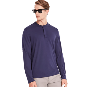 A man wearing a long-sleeve, navy blue henley shirt paired with light gray pants. He has sunglasses on and is looking to the side.