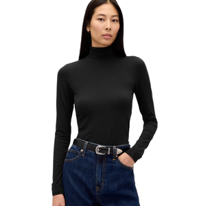 A woman is wearing a fitted black turtleneck long-sleeve top paired with high-waisted dark blue jeans and a black belt with a silver buckle.