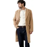 A man is wearing a tan overcoat, white shirt, dark blue jeans, and brown leather boots.