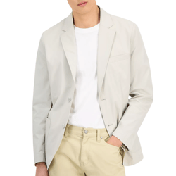 A man wearing a light gray blazer over a white T-shirt and beige pants, with one hand in his pocket.