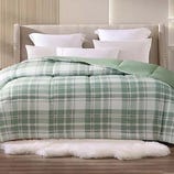 A bed with white pillows and a green plaid comforter, situated on a white fluffy rug in a modern bedroom setting.