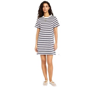 A woman is wearing a short-sleeve, black-and-white striped dress and casual beige shoes with white socks, accessorized with a small necklace.