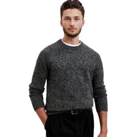 A man wears a dark gray, textured crew-neck sweater paired with black trousers. The sweater has a classic style, providing a sleek and simple look.