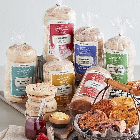 A variety of Wolferman's English muffins are displayed, including traditional, cranberry citrus, wild Maine blueberry, multigrain honey, cinnamon raisin, and San Francisco sourdough. The muffins are packaged in branded bags.