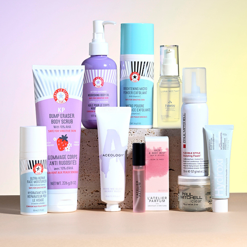 A variety of skincare and haircare products are shown, including First Aid Beauty scrubs and creams, Aceology mask, Luna Nectar serum, Paul Mitchell styling foam, and a perfume by L'Atelier Parfum.
