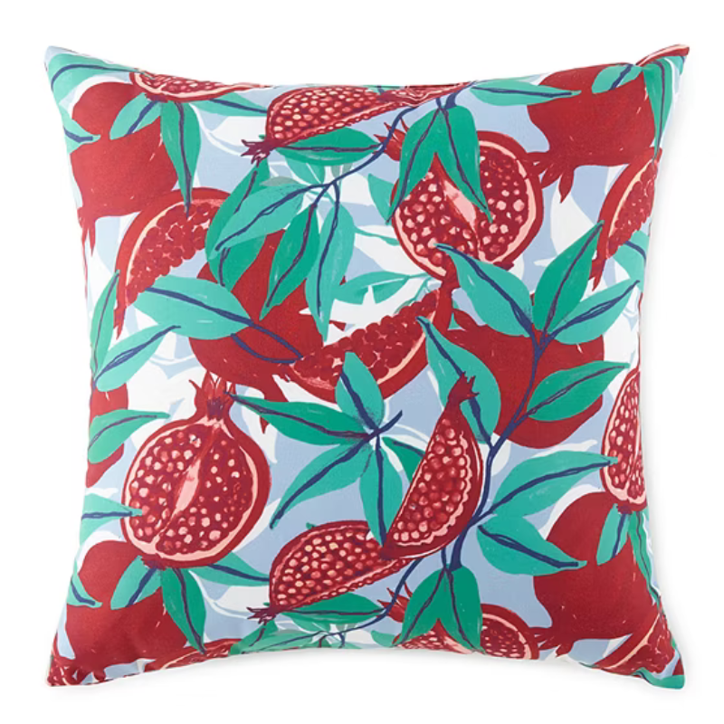 Decorative pillow featuring a colorful pattern of red pomegranates and green leaves on a light blue background.