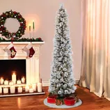 A slim, snowy artificial Christmas tree with lights is surrounded by festive gift boxes. Nearby, a decorated mantel features stockings, candles, and a wreath.
