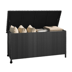 A black rattan outdoor storage box with a hinged lid, containing beige cushions and folded blankets.