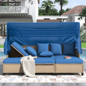Outdoor patio daybed with an adjustable backrest, blue cushions, and canopy, set on a wicker base. Includes several matching blue throw pillows and a textured beige blanket. Pool and modern house in the background.