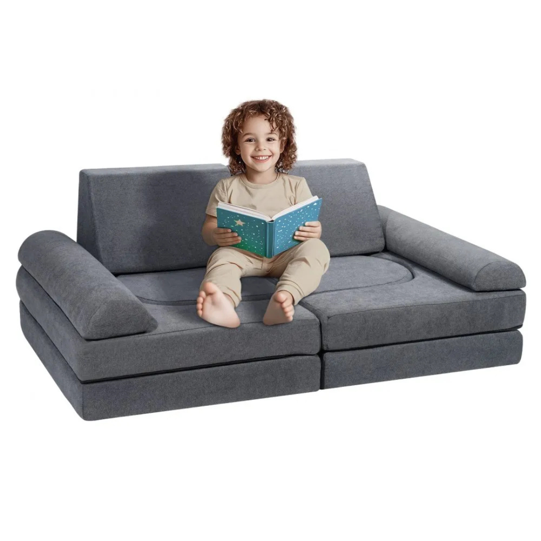 A child is sitting on a modular, gray convertible sofa reading a book. The sofa has detachable cushion sections, allowing it to be rearranged for versatility.