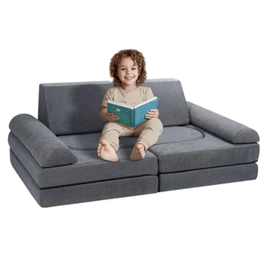 A child is sitting on a modular, gray convertible sofa reading a book. The sofa has detachable cushion sections, allowing it to be rearranged for versatility.