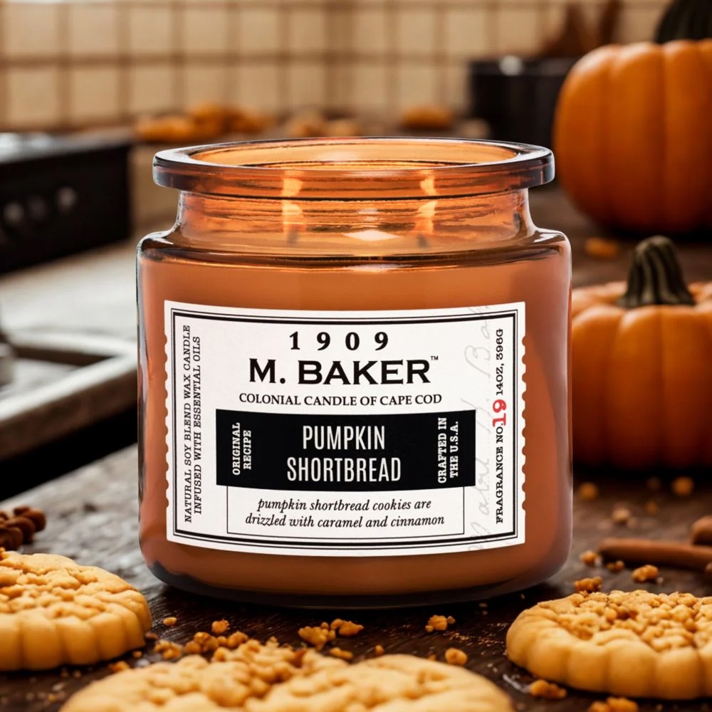M. Baker Colonial Candle of Cape Cod, fragrance \“Pumpkin Shortbread\“ with a scent of pumpkin shortbread cookies drizzled with caramel and cinnamon; accompanied by cookies and pumpkins in the background.