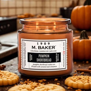 M. Baker Colonial Candle of Cape Cod, fragrance \“Pumpkin Shortbread\“ with a scent of pumpkin shortbread cookies drizzled with caramel and cinnamon; accompanied by cookies and pumpkins in the background.
