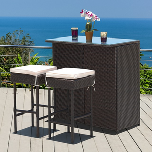 A patio bar set featuring a dark wicker bar counter with a glass top, accompanied by two matching bar stools with beige cushions, set against a scenic ocean view.