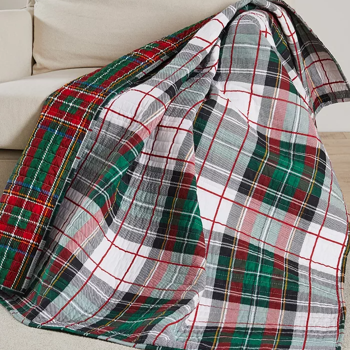 A multicolored plaid throw blanket is draped over the arm of a beige sofa.