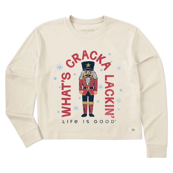 Women's long sleeve shirt with a cream color featuring a nutcracker in a red and blue uniform. The text reads \“What's Cracka Lackin'\“ with \“Life is Good\“ below. Design includes light blue snowflakes.