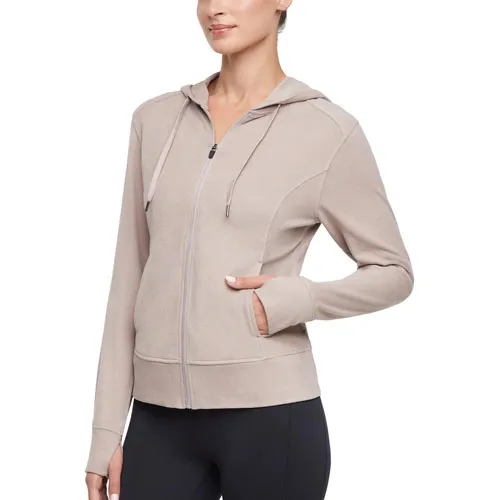 A woman is wearing a light beige zip-up hoodie with a hood and front pockets, paired with black leggings.