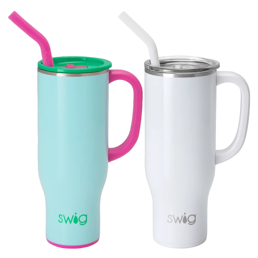 Two tall travel mugs with handles and silicone straws; one is light blue with pink and green accents, while the other is white with silver and white accents. Both feature the \“swig\“ logo at the base.