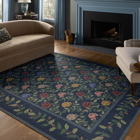 8' x 10' floral area rug with a blue background and colorful flowers, placed in a living room with neutral-toned furniture and a blue fireplace.