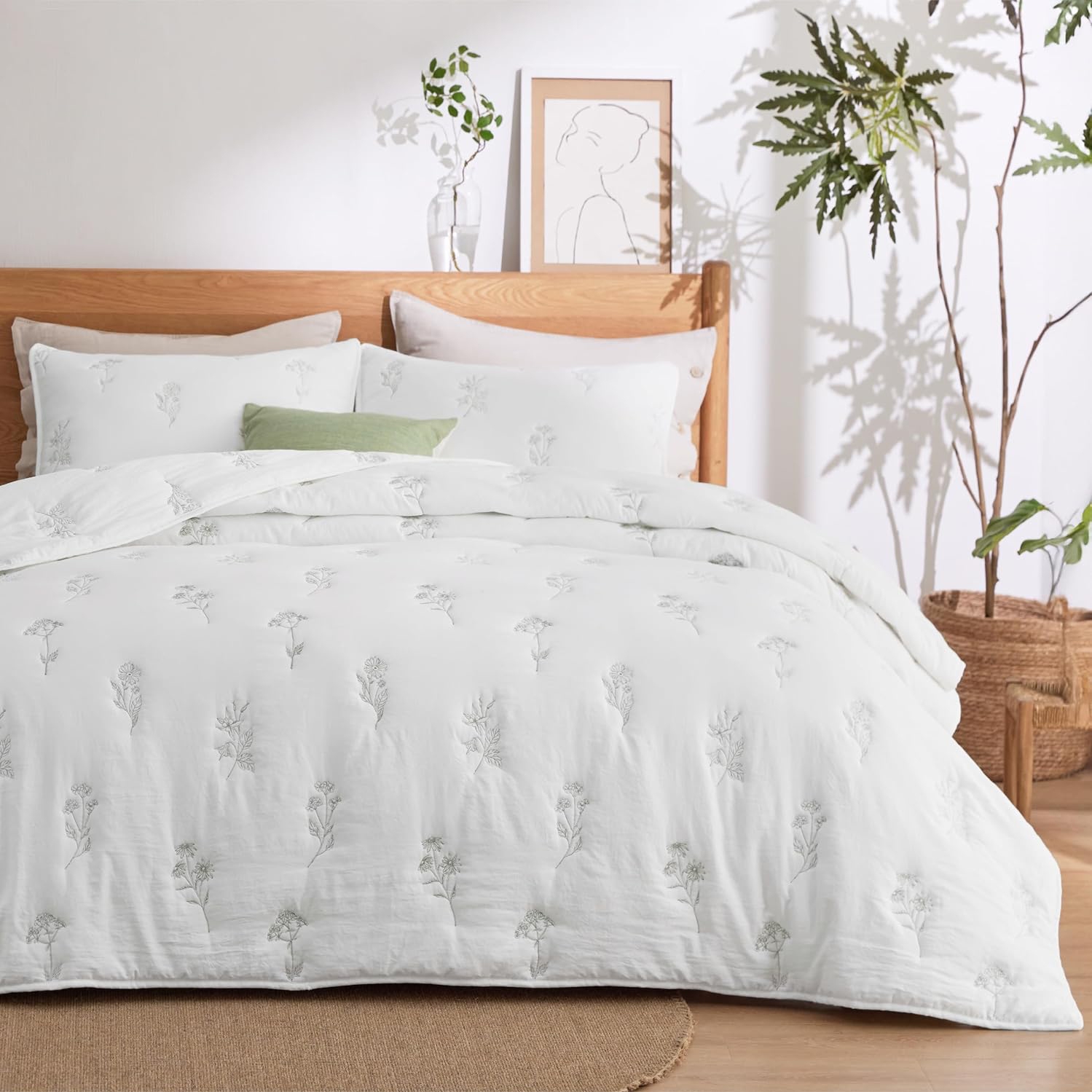 A wooden bed with a white duvet cover adorned with subtle floral embroidery, accompanied by matching pillows. A potted plant and minimalist artwork complement the serene, natural room decor.