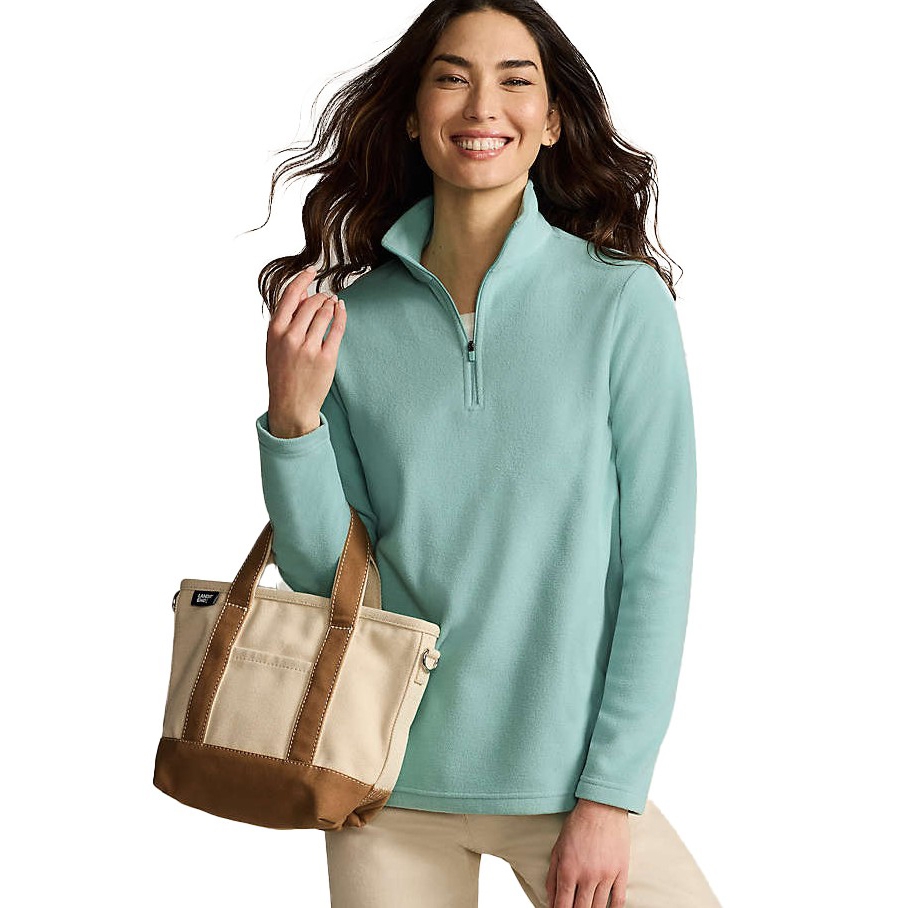 A person is wearing a light blue zip pullover fleece and carrying a beige and brown canvas tote bag.