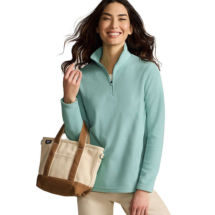 A person is wearing a light blue zip pullover fleece and carrying a beige and brown canvas tote bag.