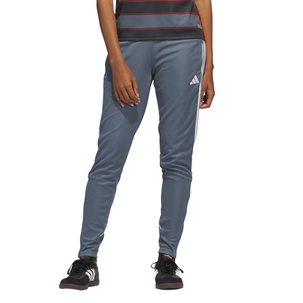 A person wearing gray Adidas track pants with white stripes and black Adidas shoes.