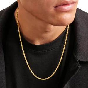 A person is wearing a gold rope chain necklace with a black shirt and dark outerwear.
