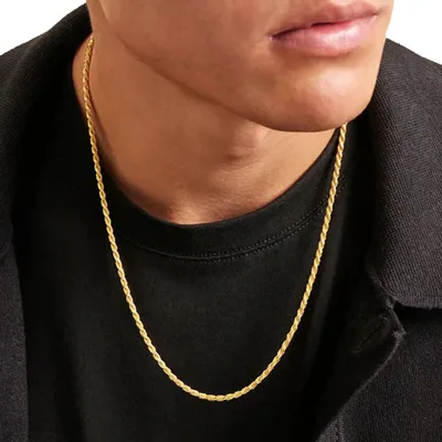 A person is wearing a gold rope chain necklace with a black shirt and dark outerwear.