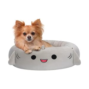 A small dog is sitting in a gray, plush pet bed designed to resemble a smiling cartoon character.