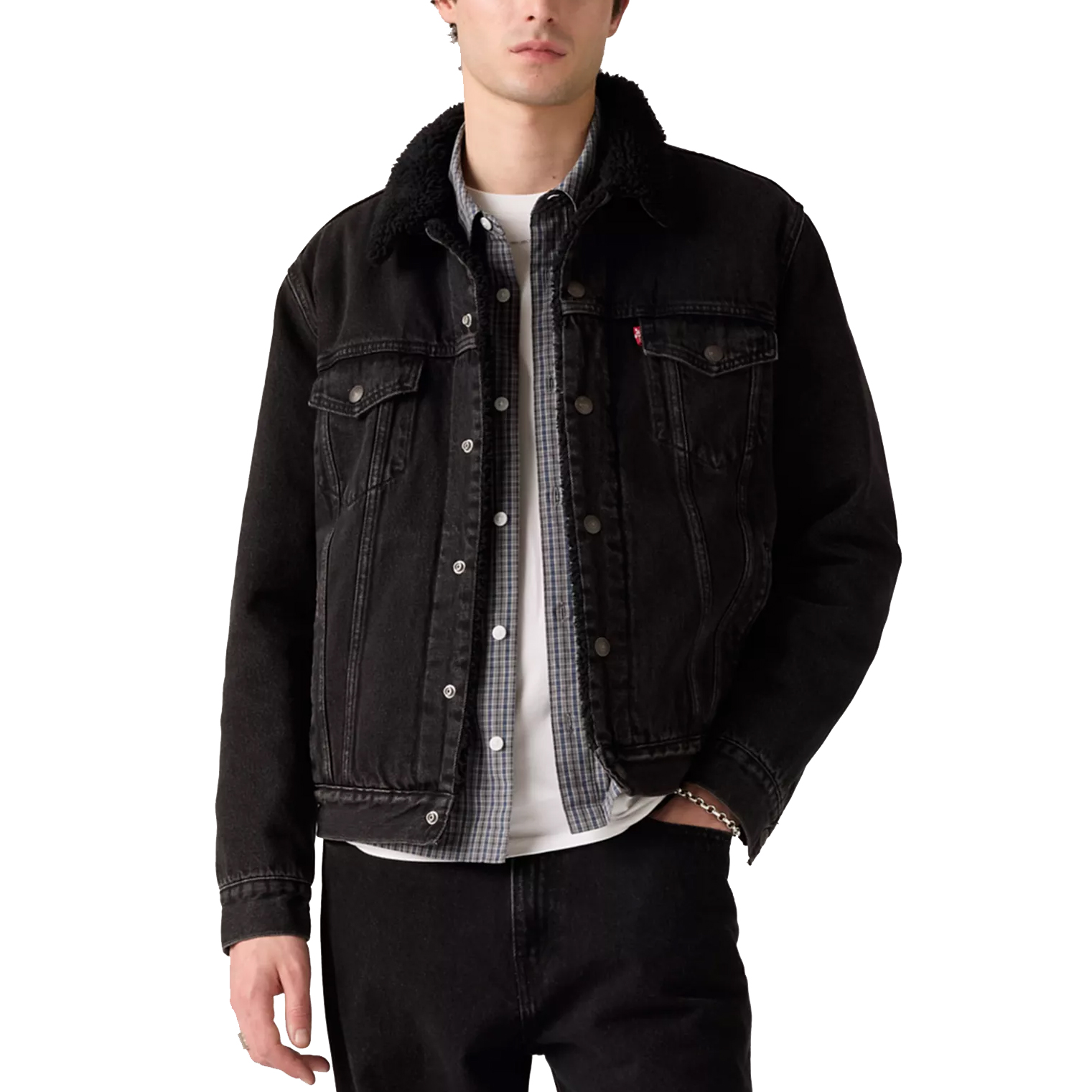 A man wears a black denim jacket with a shearling collar, layered over a plaid shirt and a white T-shirt.