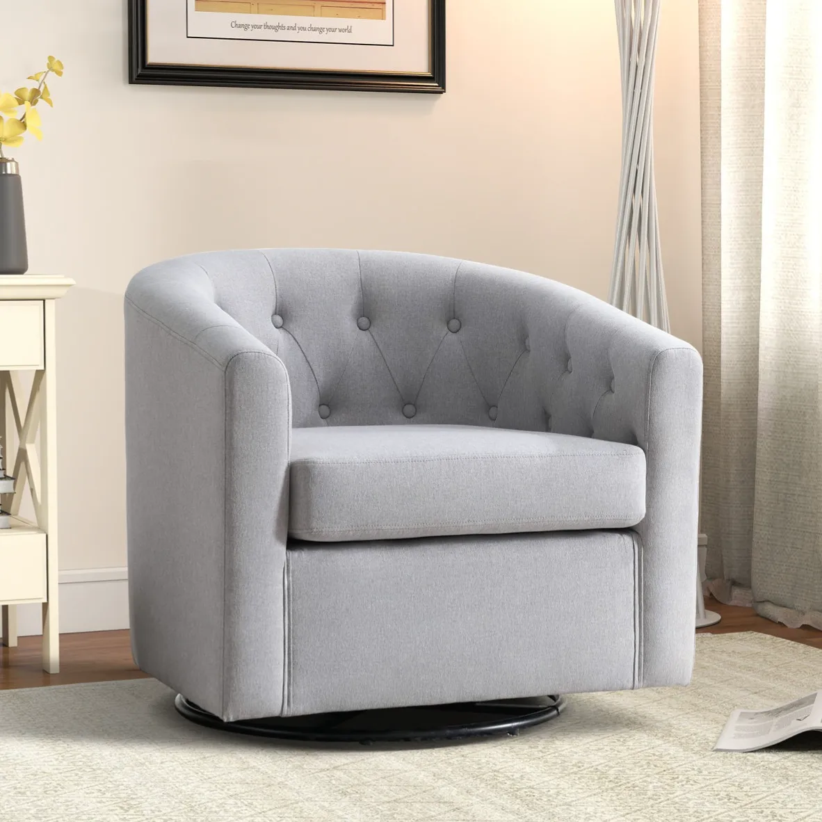 A gray swivel barrel chair with tufted detailing, set on a round base. It's positioned beside a cream-colored side table with books and a vase.