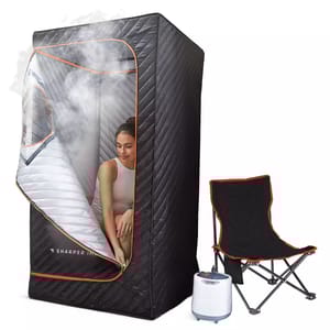 A portable sauna tent with a quilted black exterior and a zippered opening, containing a steam generator and accompanied by a black folding chair with orange trim.