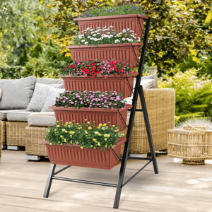 A tiered plant stand features five terracotta-colored rectangular planters stacked vertically, each filled with different colorful flowers, supported by a black metal frame. It's set on a patio with wicker furniture in the background.