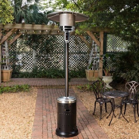 Outdoor patio heater with a round table and overhead reflector, next to a metal bistro set in a garden.