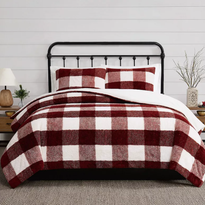 Red and white checkered bedding set on a bed with a black metal frame, accompanied by wooden bedside tables and simple decor.