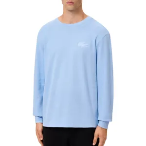 A light blue long-sleeve crewneck shirt with a subtle embroidered logo on the left chest, paired with black pants.