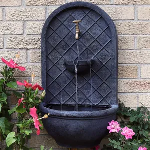 A wall-mounted outdoor water fountain with a brass spigot, accented by blooming pink flowers.