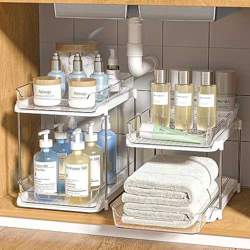 Two tiered, sliding clear plastic cabinet organizers are shown storing various bottles and towels under a sink.