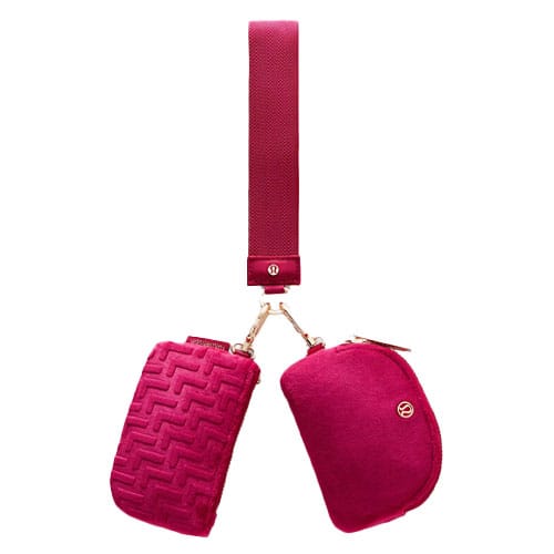 Magenta crossbody bag with two zippered pouches, one featuring a textured pattern. The strap connects to the pouches with gold hardware.