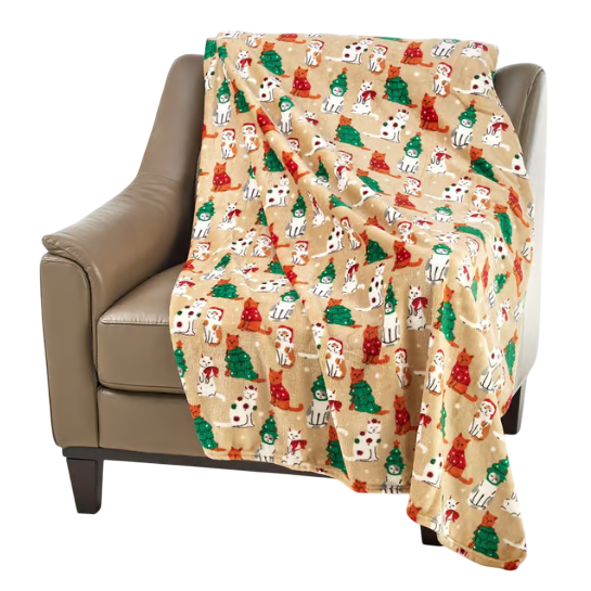 A tan blanket with a festive print featuring cartoon dogs in holiday attire and green and red trees is draped over a beige armchair.