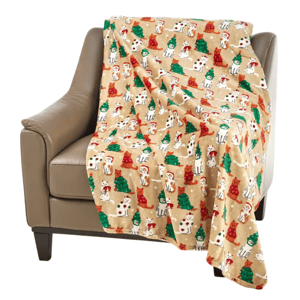 A tan blanket with a festive print featuring cartoon dogs in holiday attire and green and red trees is draped over a beige armchair.